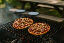 Grilled flatbreads topped with BBQ chicken, melted cheese, and fresh herbs over a campfire.