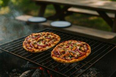 Grilled flatbreads topped with BBQ chicken, melted cheese, and fresh herbs over a campfire.