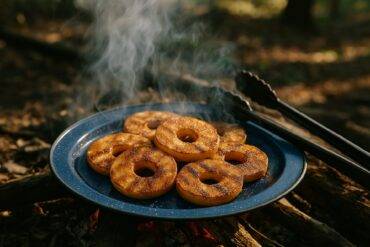 Apple rings coated in cinnamon sugar cooking over a campfire grate.