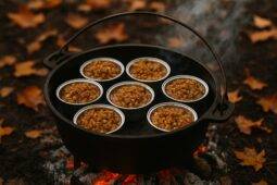 Small apple crisp bites with a crumbly topping in a black cast-iron Dutch oven over campfire coals.