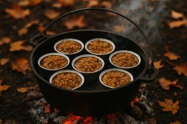 Small apple crisp bites with a crumbly topping in a black cast-iron Dutch oven over campfire coals.