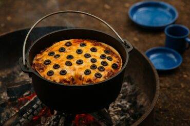 A cheesy enchilada casserole with beef and beans cooked in a Dutch oven over a campfire.