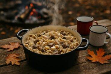Creamy turkey and wild mushroom stroganoff simmering in a black Dutch oven over a campfire.