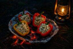 Two colorful bell peppers stuffed with a vegetable and feta cheese mixture, roasted over a campfire.