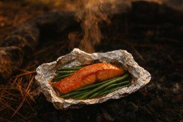Salmon fillet and green beans coated in maple Dijon sauce wrapped in foil ready for grilling.