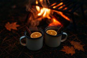 A warm bourbon drink with maple and cinnamon spices served in a mug beside cinnamon sticks and maple syrup.