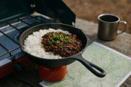 Korean beef bowl with rice and vegetables cooking on a portable propane stove outdoors.