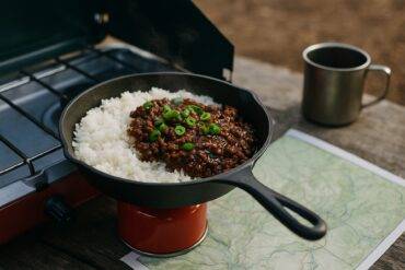 Korean beef bowl with rice and vegetables cooking on a portable propane stove outdoors.