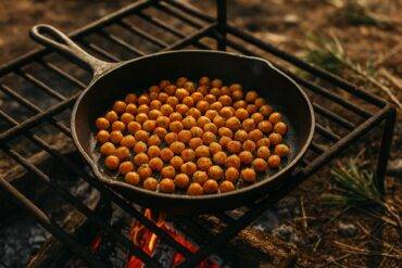 Smoky roasted chickpeas seasoned with spices in a camping skillet over a campfire grill.