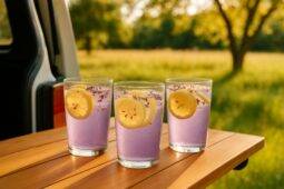 A refreshing lavender lemonade spritz in a clear glass with ice and a sprig of lavender on a camping table.